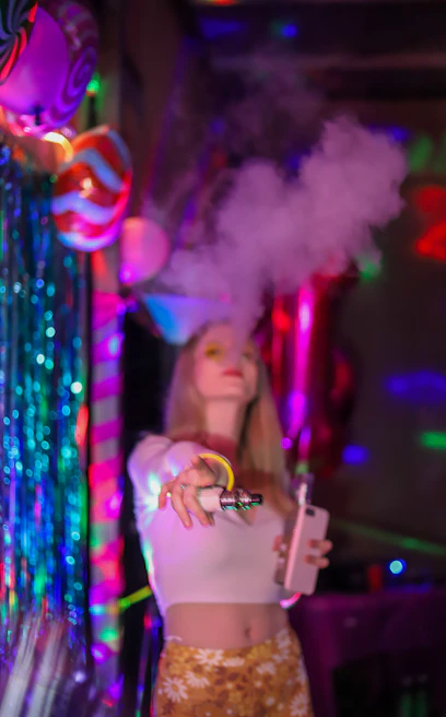A group of friends enjoying vapers with neon-colored smoke swirling around them in a cozy urban setting