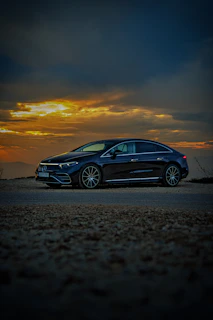 Sleek black luxury sedan parked on a coastal road at sunset