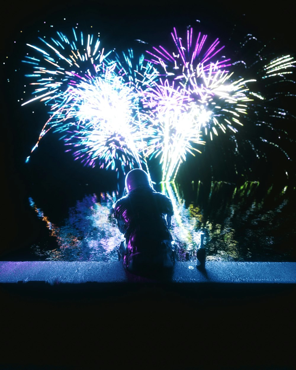 a person sitting on a ledge watching fireworks