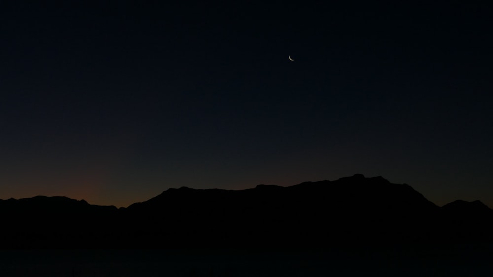 the moon is setting over a mountain range