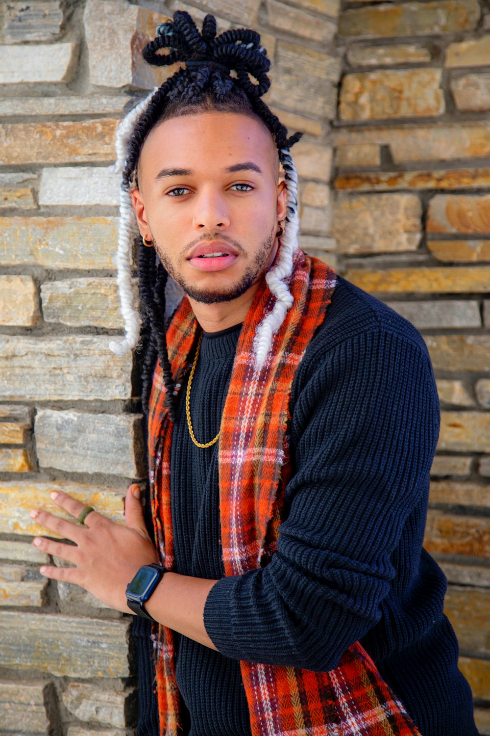 a man with dreadlocks standing in front of a brick wall