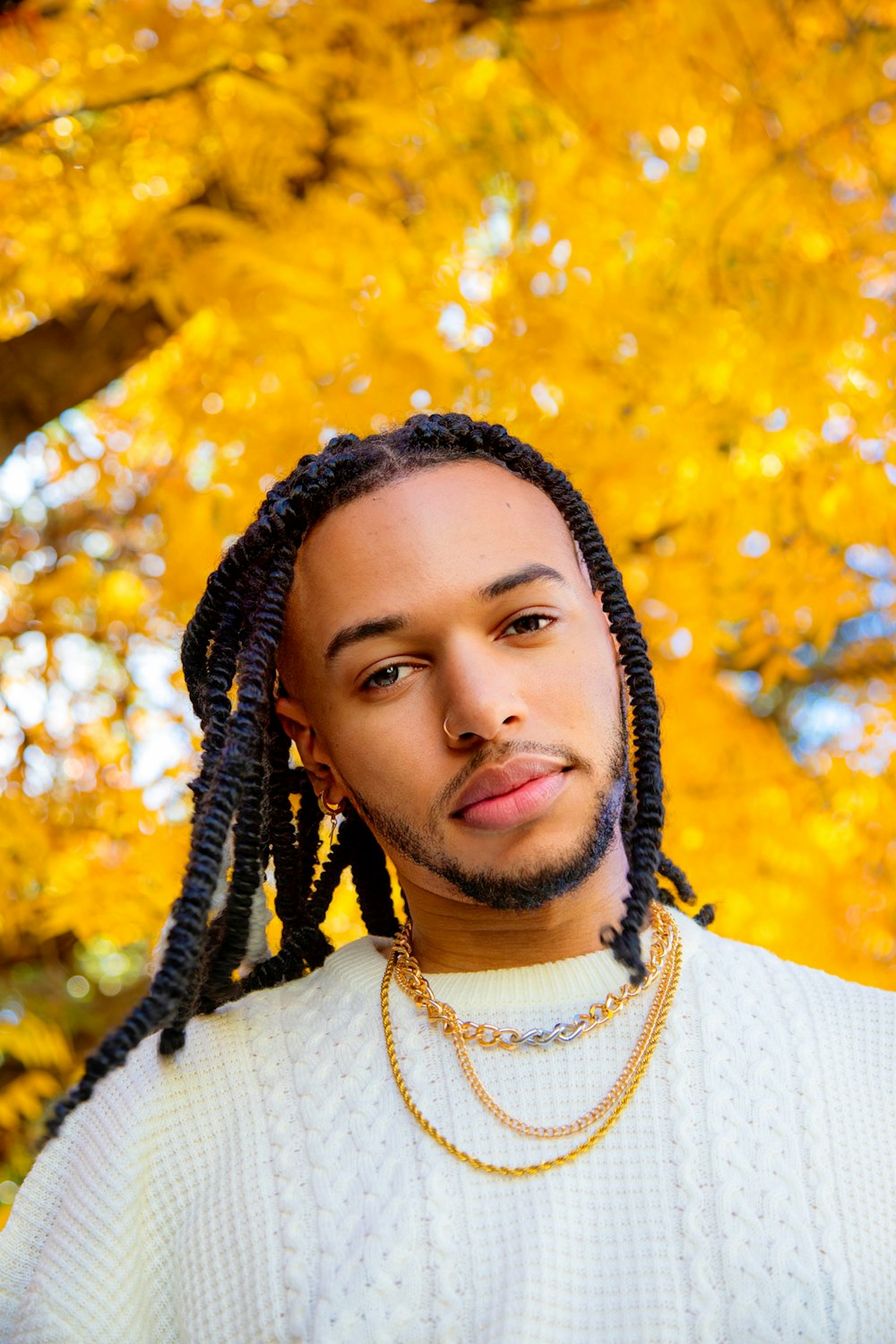 a man with dreadlocks standing in front of a tree