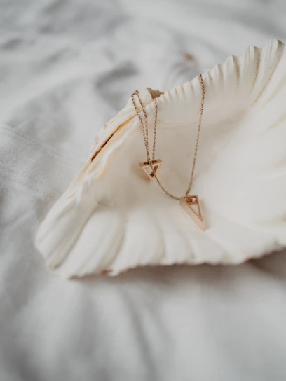 Close-up of a delicate gold and blush pink necklace resting on sunlit white sand by the ocean.