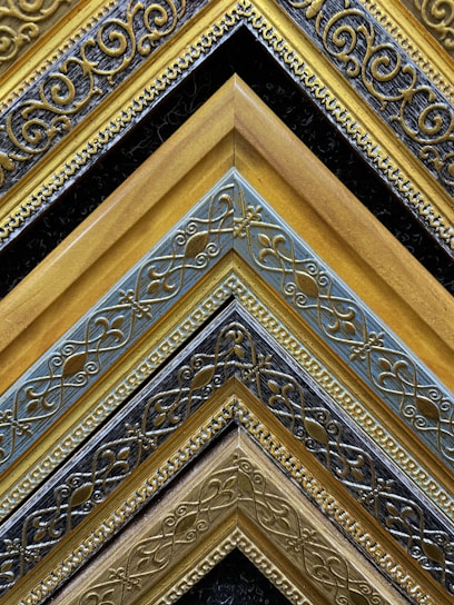 A collection of intricately designed, ornate picture frames arranged in a pattern. The frames exhibit detailed, swirling patterns with gold, silver, and black colors creating a striking visual contrast. The repetitive geometric layout emphasizes the craftsmanship and artistry.