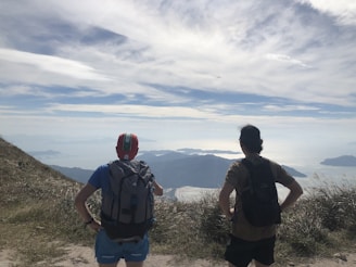 Two friends laughing together with backpacks, standing on a scenic mountain overlook at sunset.