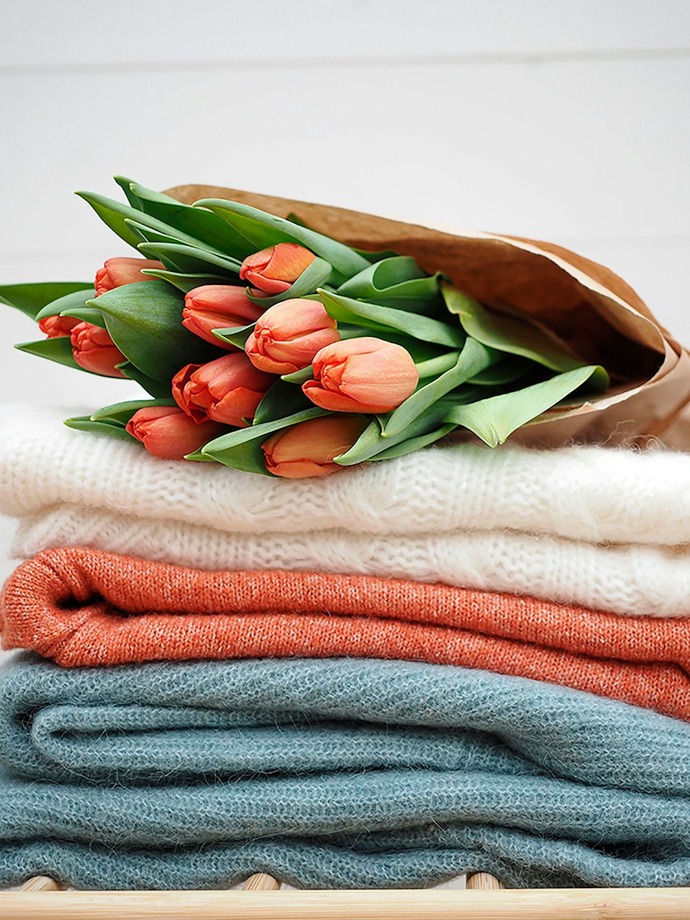 un bouquet de tulipes posé sur une pile de pulls