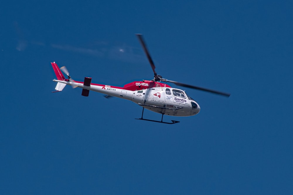 a red and white helicopter flying through a blue sky