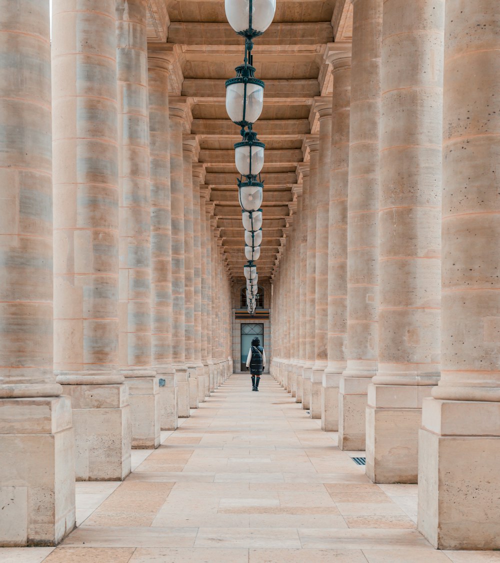 a man walking down a long hallway between two stone pillars