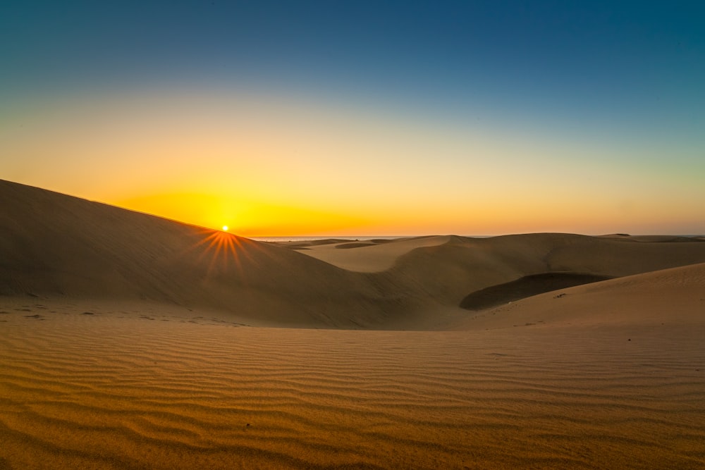 the sun is setting over the sand dunes