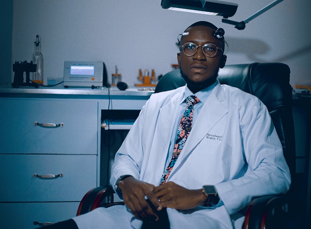 a man in a lab coat and tie sitting in a chair