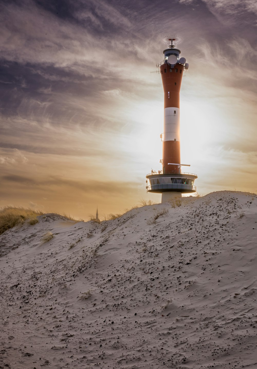 a red and white light house sitting on top of a sandy hill