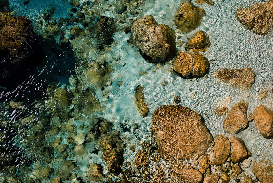 an aerial view of rocks and water in the ocean, fake drone shot from a bridge