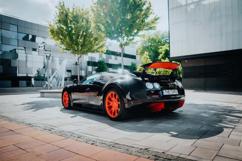 Ein schwarzer Sportwagen mit orangefarbenen Felgen parkt auf einer Straße