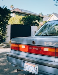 A Honda car with a Washington state license plate parked in a residential area. The back of the car is prominently visible, including the taillights and badges. In the background, there are houses with greenery and a black gate.