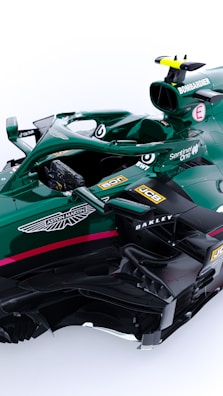 A green Formula 1 racing car with various sponsor logos including Aston Martin, Bombardier, JCB, Oakley, BWT, and SentinelOne. The car features intricate aerodynamic components and a sleek design. It has a single cockpit with a visible steering wheel and control mechanisms.