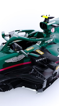 A green Formula 1 racing car with various sponsor logos including Aston Martin, Bombardier, JCB, Oakley, BWT, and SentinelOne. The car features intricate aerodynamic components and a sleek design. It has a single cockpit with a visible steering wheel and control mechanisms.