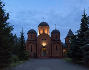 A serene evening shot of the church building softly illuminated, inviting all to join in fellowship and worship.