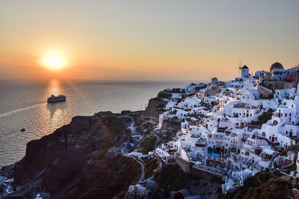 the sun is setting over a small village on a cliff