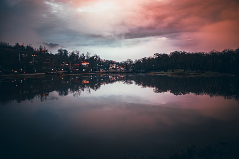 a body of water surrounded by trees under a cloudy sky