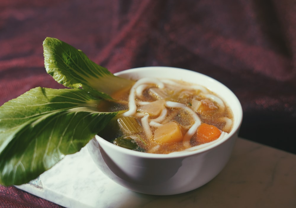 a bowl of soup with noodles, carrots and lettuce
