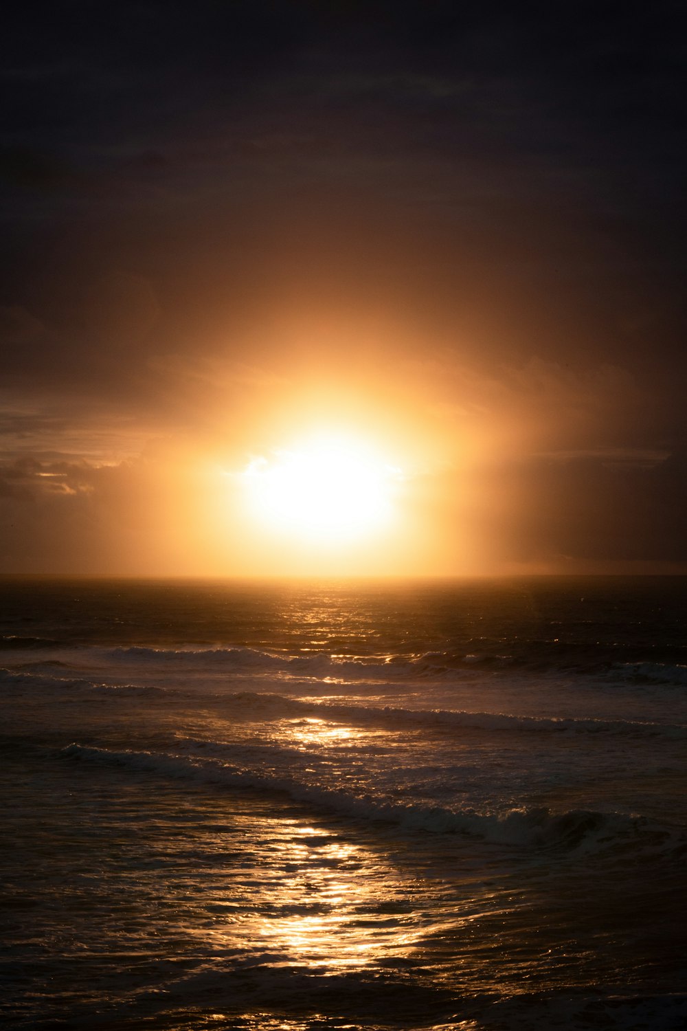 the sun is setting over the ocean on a cloudy day