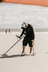 An adult using a professional metal detector along a rocky shoreline.