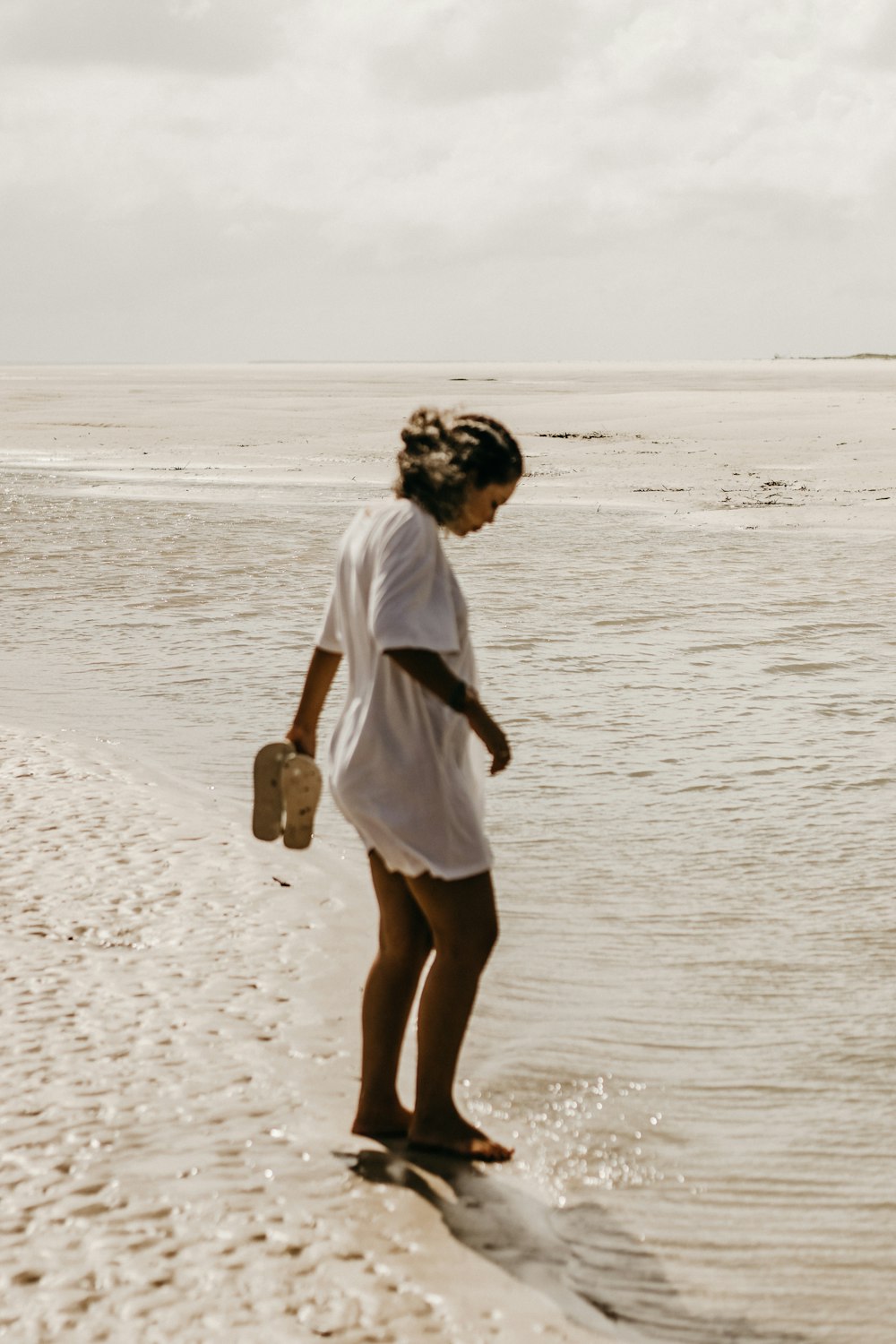 Una donna in piedi su una spiaggia accanto a uno specchio d'acqua