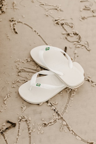 a pair of white slippers laying on top of a beach