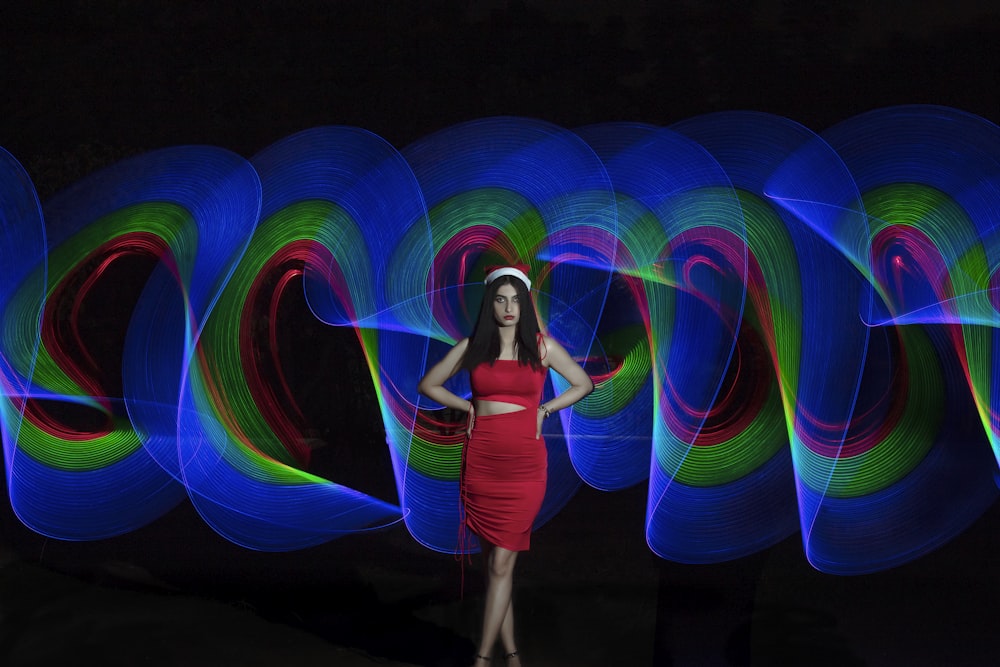 a woman in a red dress standing in front of a wall of colorful lights