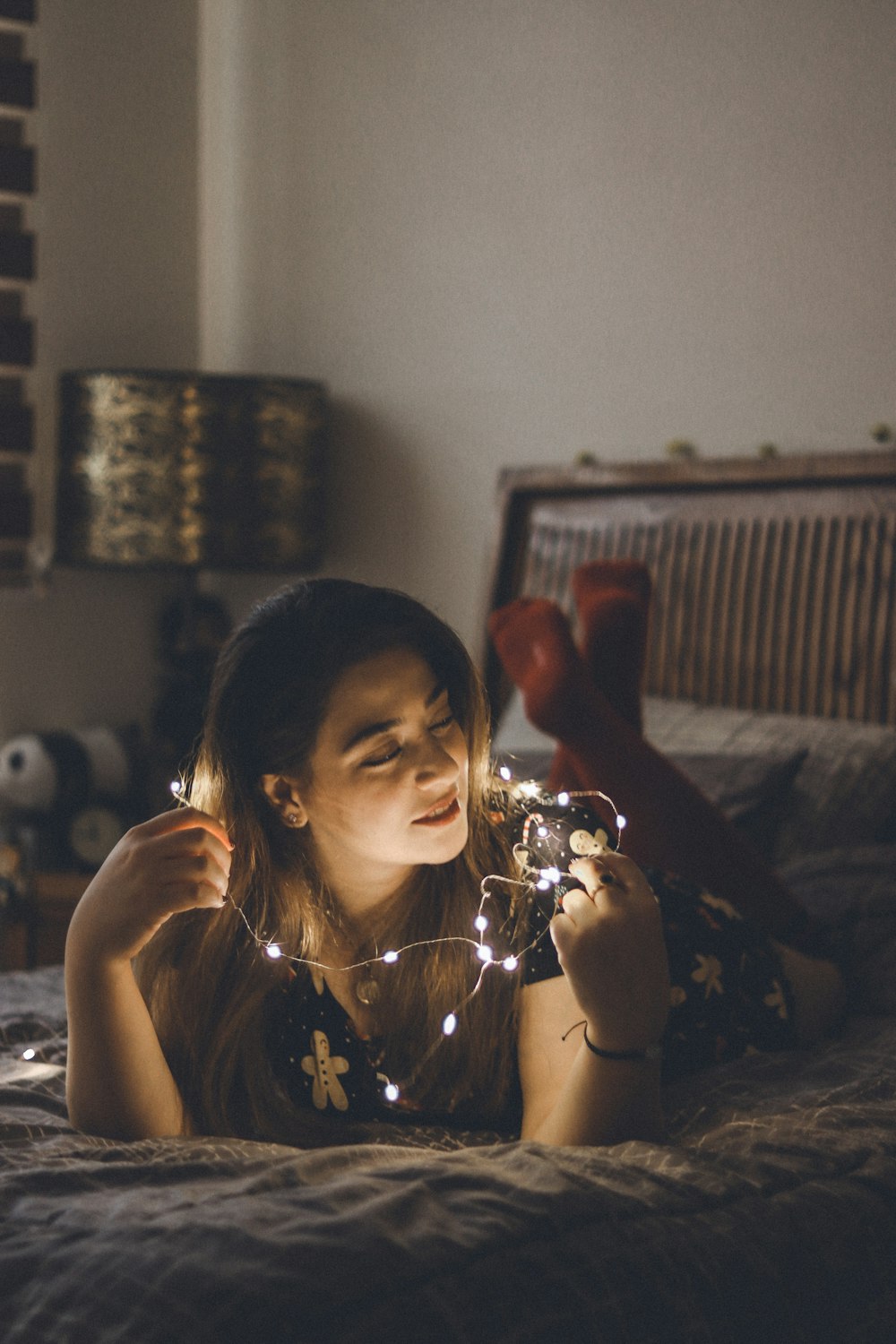 a girl laying on a bed holding a string of lights