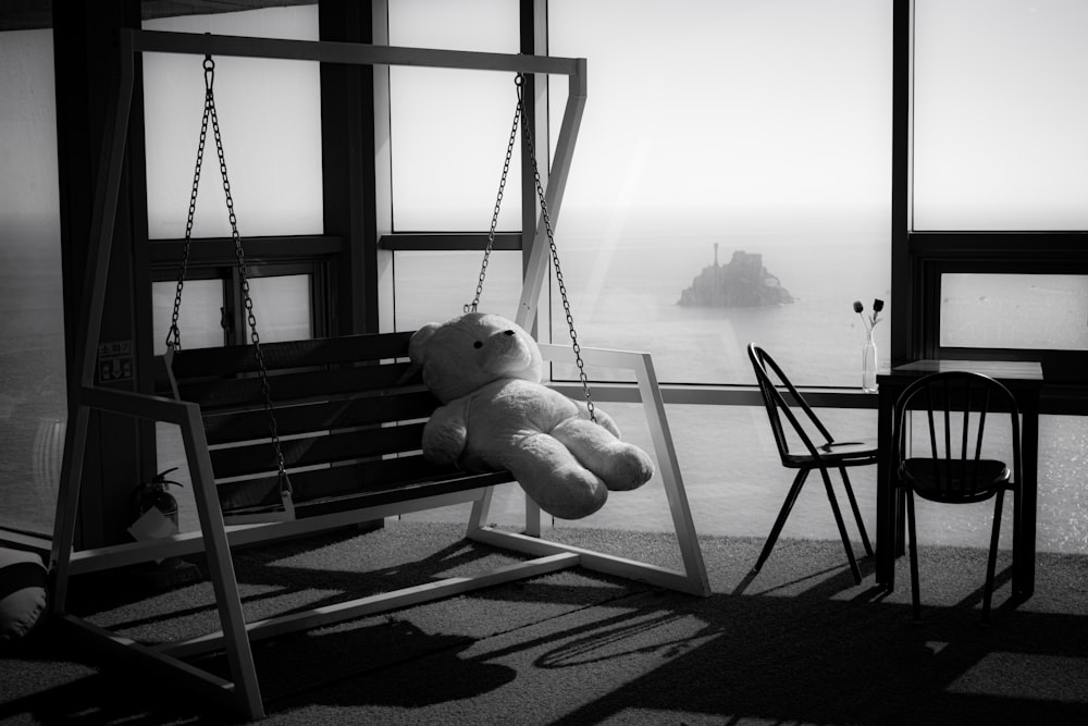 a teddy bear sitting on a swing in front of a window