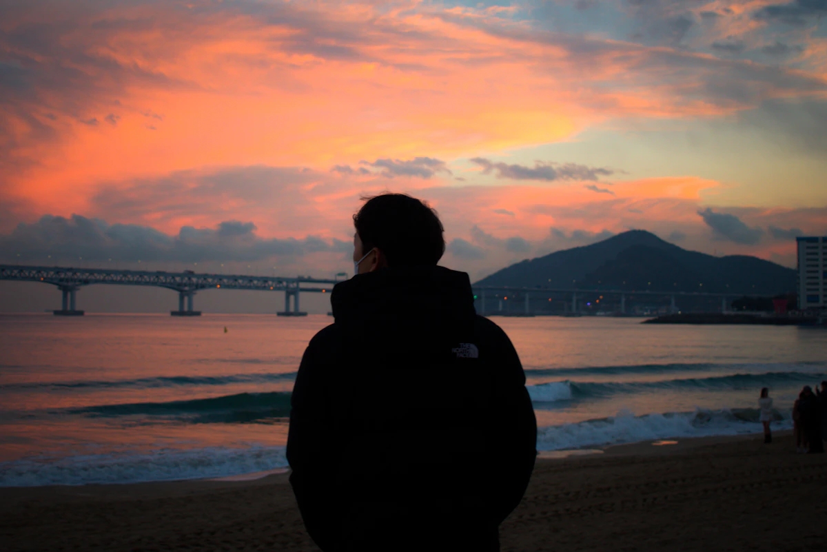 Silhouette of a person from behind on Gwangalli Beach at sunset, Gwangan Bridge across the bay