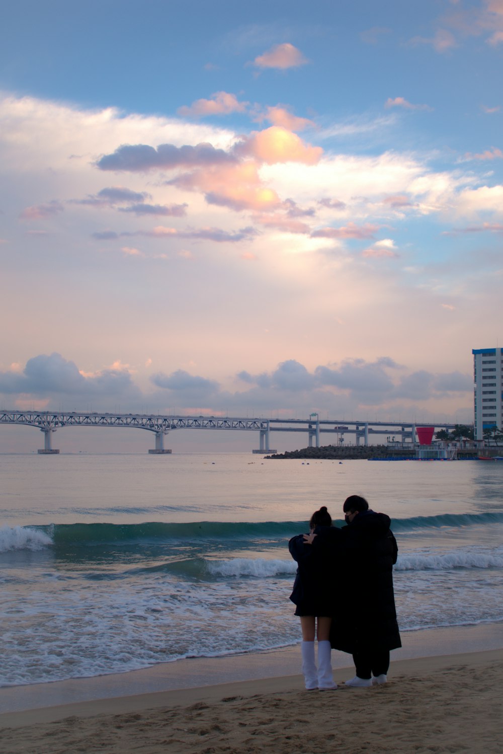 a man and a woman standing on a beach next to the ocean