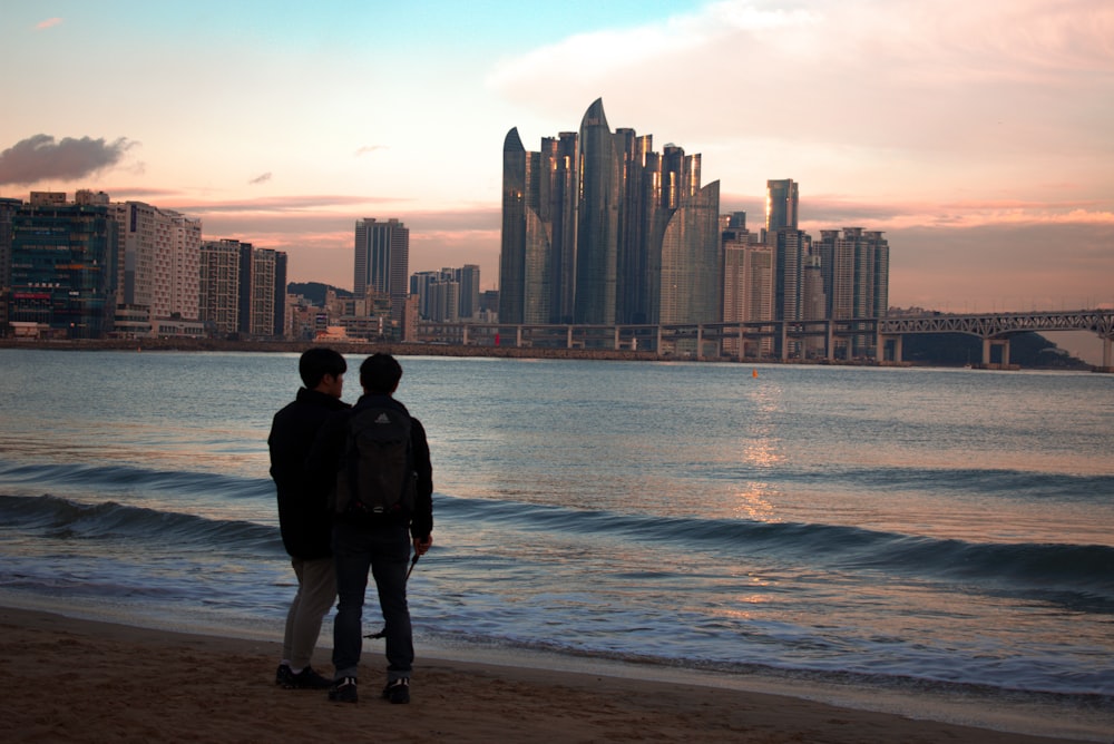 two people standing on a beach near the ocean