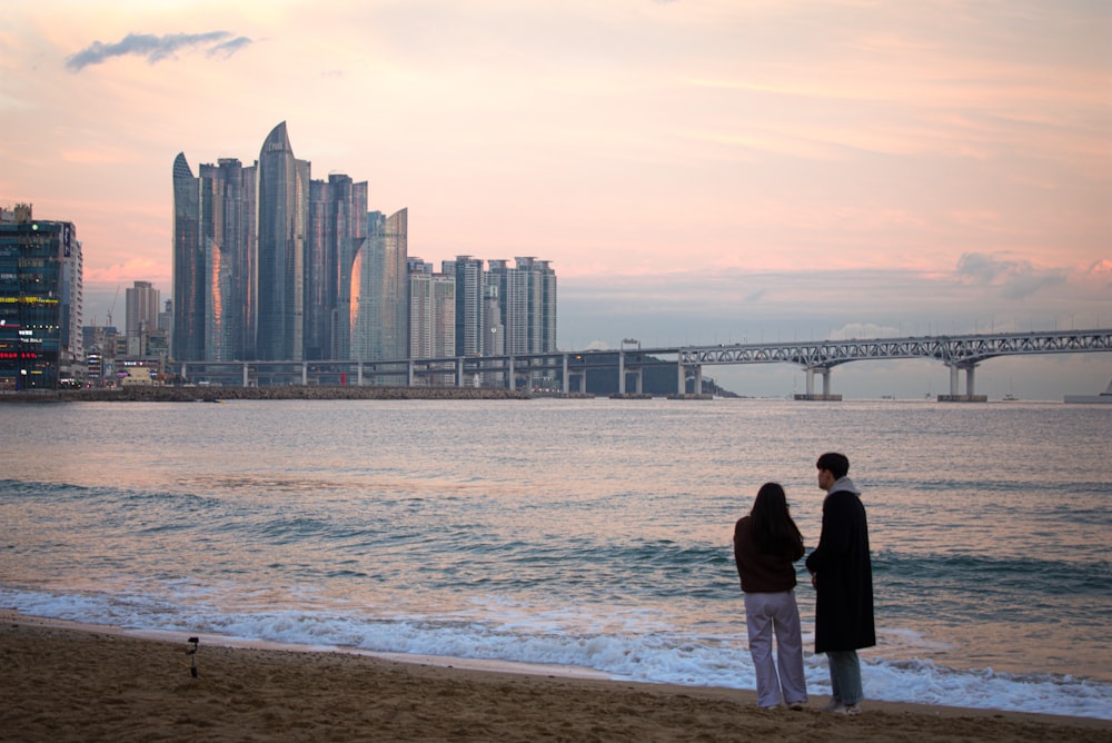 a man and a woman standing on a beach next to the ocean