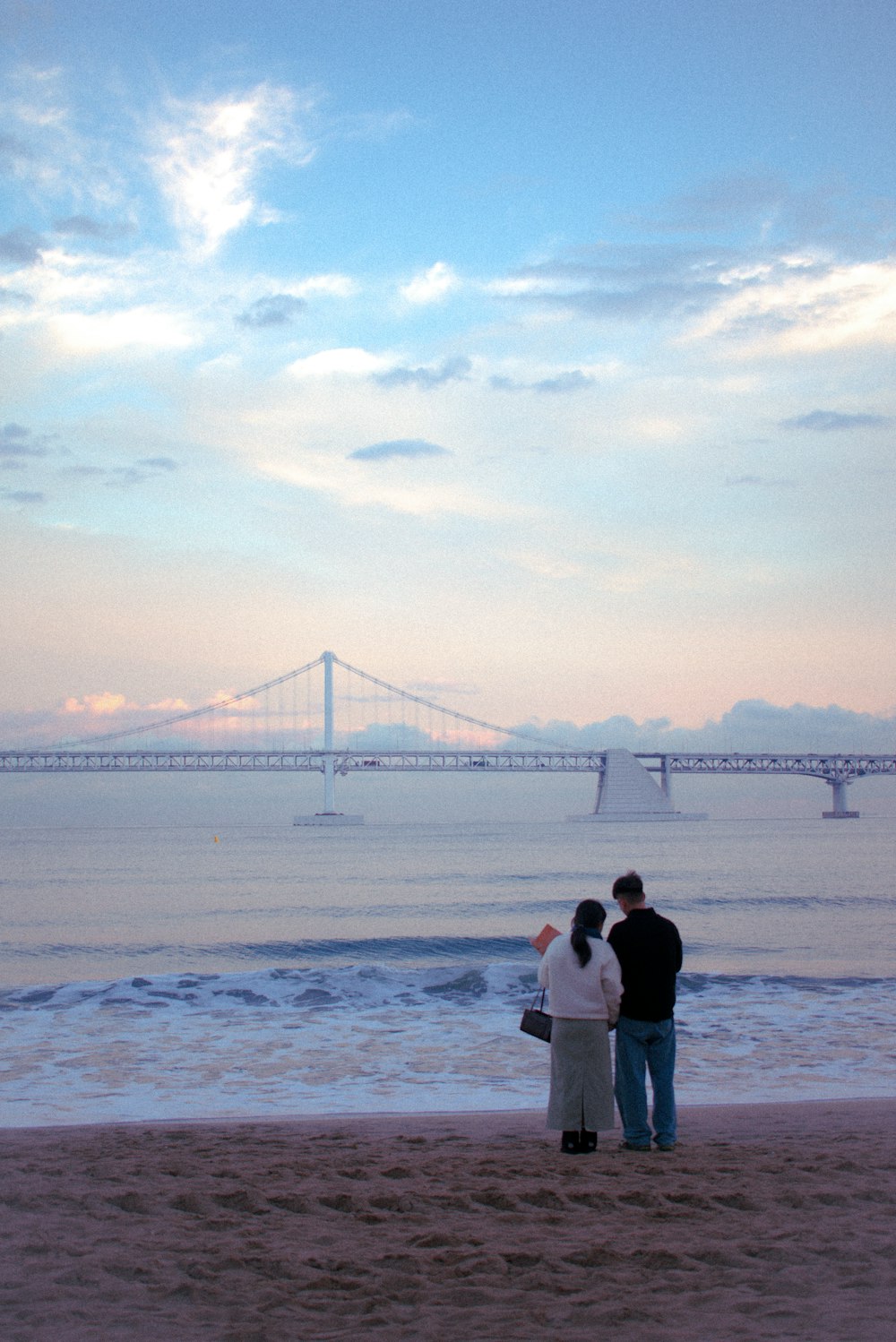 a man and a woman standing on a beach next to the ocean