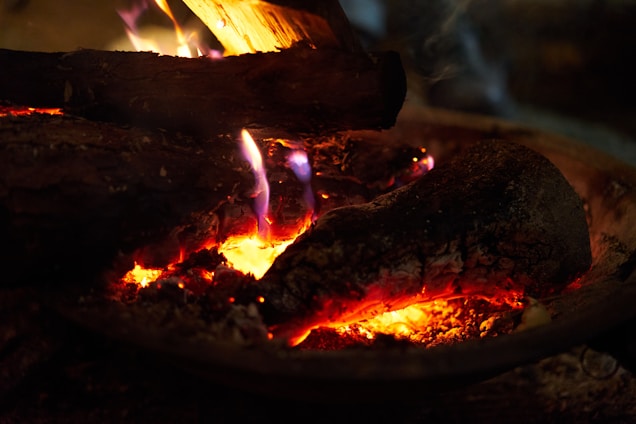 Logs of wood are burning with visible flames and embers. The fire illuminates the surrounding area with a warm glow.