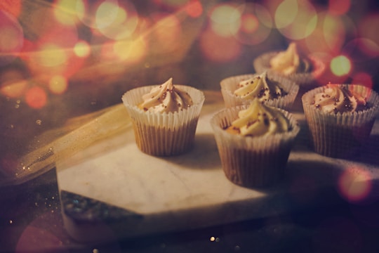 Cupcakes with creamy frosting and sprinkles are arranged on a marble board, surrounded by a soft, warm bokeh effect in the background.