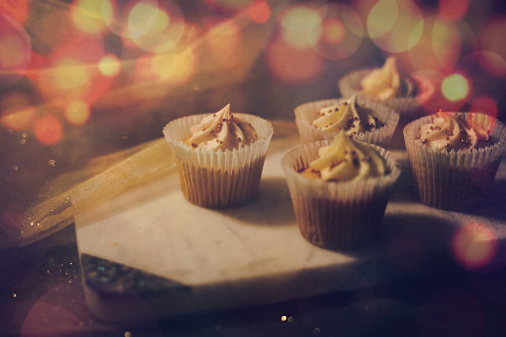 a wooden cutting board topped with cupcakes on top of a table