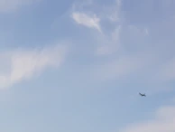A small plane soaring above patchwork fields under a clear blue sky.