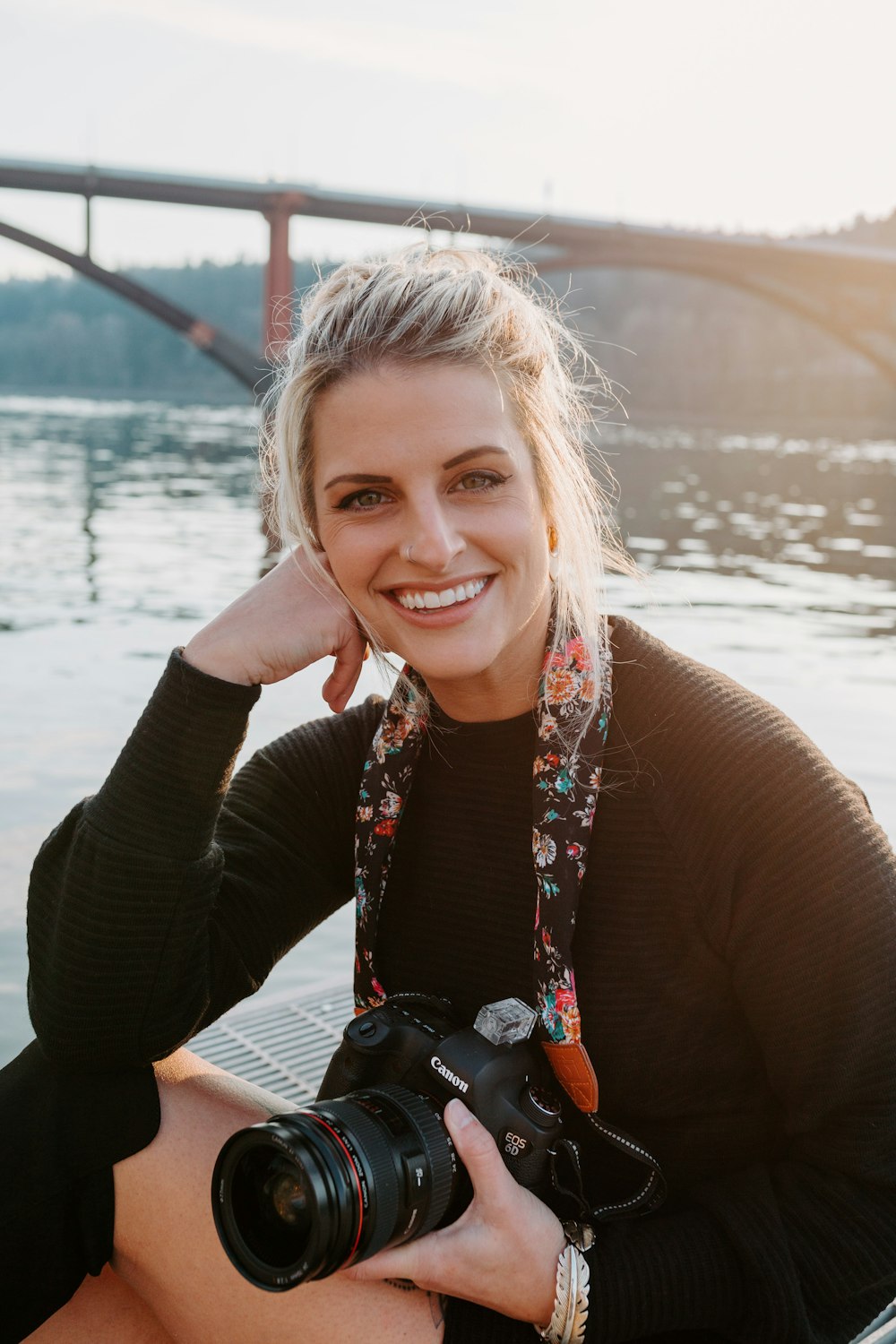 a woman sitting next to a body of water holding a camera