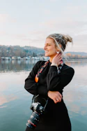 a woman with a camera standing by a body of water