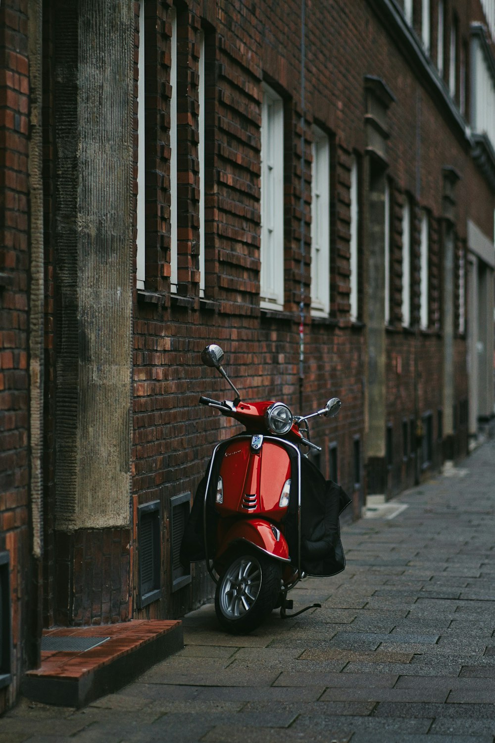 a red scooter parked next to a brick building