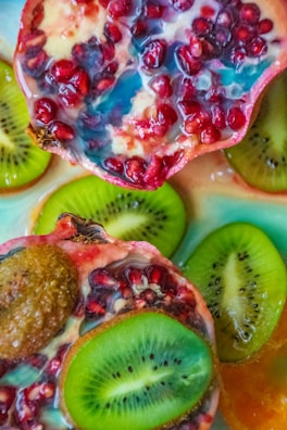 Close-up of a vibrant fruit cup with colorful slices of mango, kiwi, and pomegranate against a black background.