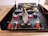 A detailed view of an electronic circuit board with various components including capacitors, resistors, connectors, and colored wiring. The board is housed within a metallic or plastic case, and includes multiple red and black terminal connectors, as well as larger circular connectors.