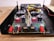 A detailed view of an electronic circuit board with various components including capacitors, resistors, connectors, and colored wiring. The board is housed within a metallic or plastic case, and includes multiple red and black terminal connectors, as well as larger circular connectors.