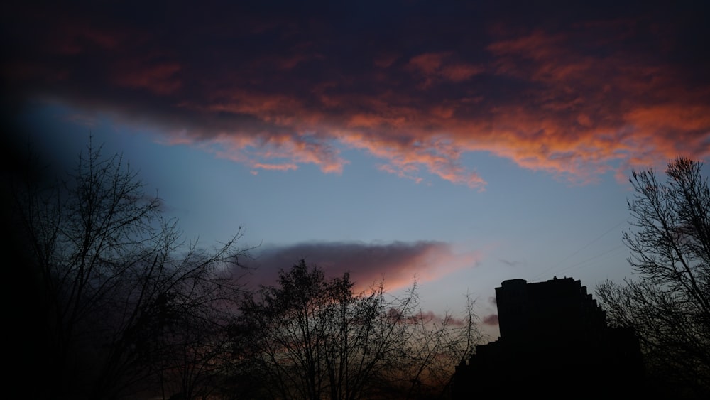 a dark sky with clouds and trees in the foreground