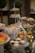 A lavish buffet setup featuring tiered trays filled with various sweets and appetizers. The trays contain cupcakes, fruits like grapes and watermelon, and small desserts. Decorative greenery and lights adorn the table, adding a festive atmosphere. Two topiary trees are visible in the background, enhancing the elegant presentation.