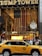 The entrance to a large building is adorned with a massive American flag and features gold-toned lettering above the entrance. A traditional clock is situated on the right, with decorative figures of soldiers on either side. A yellow taxi is driving past, while a crowd of people gathers near the entrance.