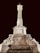 A grand, illuminated stone monument features an ornate, tall column with intricate carvings. At the base, two seated statues are positioned on either side, adding to the monument's majestic appearance. The dark night sky provides a stark contrast, emphasizing the monument's details.